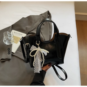 Detail of black glossy leather bucket bag with pearl lace bow charm and shoulder strap
