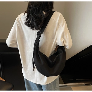 Detail of a black crescent crossbody bag with an adjustable wide strap worn by a model