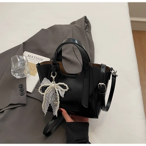 Detail of glossy black leather bucket bag with white lace bow charm on a grey blazer