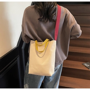 Détail du sac cabas en toile avec poignées jaunes et bandoulière rouge sur modèle