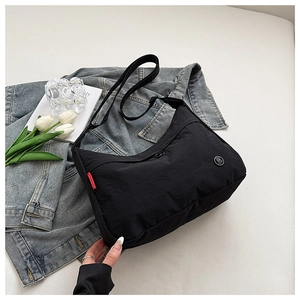 Detail of black nylon hobo bag with red woven label and round badge in a casual setting