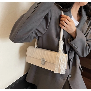 Dettaglio borsa baguette crema con fibbia metallica e nastro in pizzo su blazer