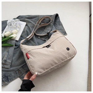 Detail of beige nylon crossbody bag with side red label on casual denim background
