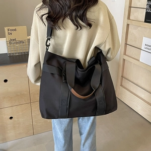Large black canvas tote bag with brown leather handles and wide strap for travel use