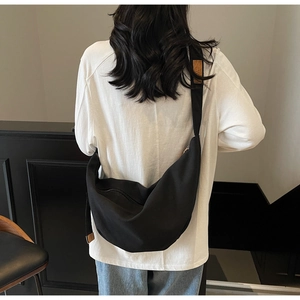 Detail of a black canvas crescent crossbody bag with brown leather patch on strap
