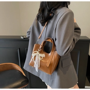 Detail of caramel glossy bucket bag with pearl lace bow charm and crossbody strap