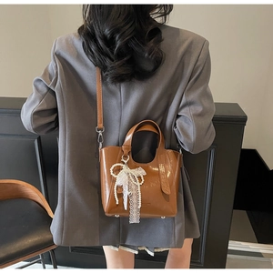 Brown leather bucket bag styled with pearl lace bow charm on a model in profile