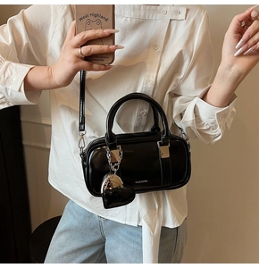 Detail of black glossy Boston bag with silver logo and heart charm on a shoulder strap