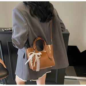 Detail of a brown bucket bag showing the white lace bow and faux pearl decoration