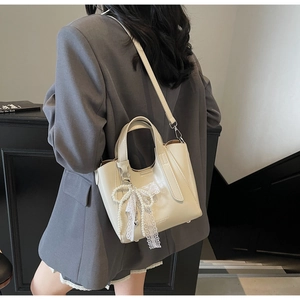 Detail of cream glossy bucket bag with pearl and lace bow charms on a grey suit jacket