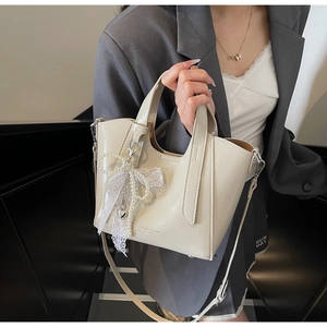 Close-up of beige glossy bucket bag featuring lace bow charm and heart metal pendant