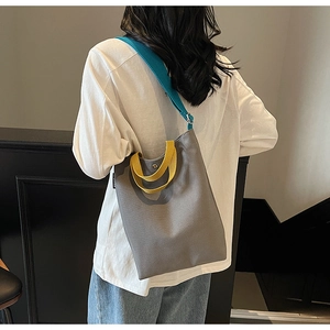 Détail du sac seau en toile contrastée avec poignée jaune et bandoulière bleue large