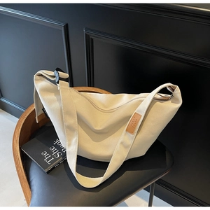 Detail of beige canvas dumpling bag with adjustable strap and leather brand label
