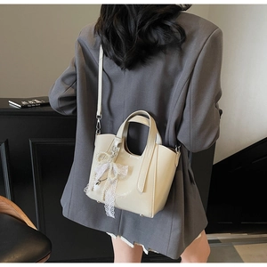 Close-up of beige bucket bag with pearl lace bow charm and premium polished texture
