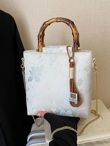 Elegant floral lace handbag with bamboo handle and golden chain strap in a studio setting