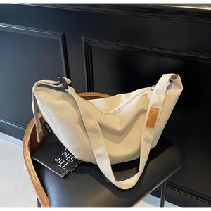 Detail of off-white canvas crescent bag with leather logo tag on a black leather chair