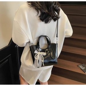 Detailed view of black patent leather bucket bag with elegant pearl lace bow pendant charm