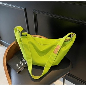 Macro view of neon green canvas crossbody bag featuring adjustable strap and leather label