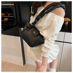 Detailed view of black pleated strap shoulder bag worn by model in a home setting