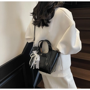 Detail of glossy black handbag with delicate white lace and pearl bow charm accessory
