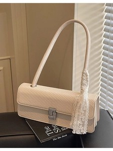 Borsa a spalla color crema con chiusura in metallo e nastro di pizzo su superficie nera