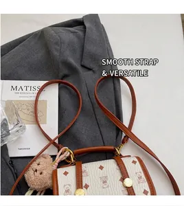 Detail of cream crossbody bag featuring bear prints, top handle, and plush charm accessory