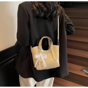 Beige glossy bucket bag with lace bow and pearl charm shown on a chic female model