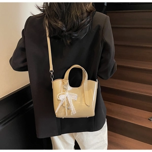 Detail of cream patent leather bucket bag with lace bow and pearl charm accents