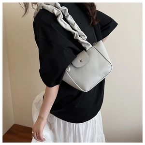 Detail of light gray pleated cloud strap and magnetic flap on a stylish leather handbag