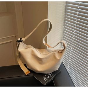Detailed macro view of beige canvas half-moon bag with elegant brown leather trim accents