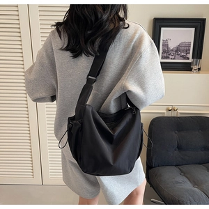 Detail of black nylon messenger bag featuring adjustable wide strap and drawstring side