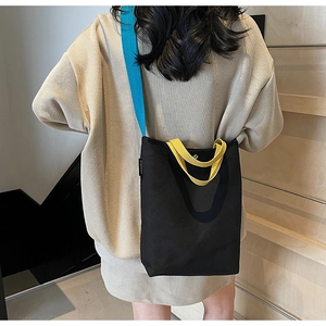 Détail du sac cabas en toile avec bandoulière bleue et poignée jaune sur un escalier