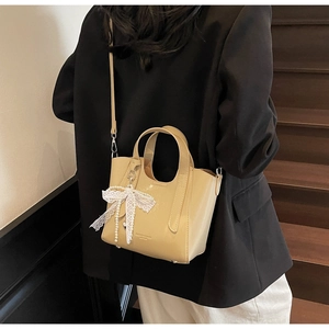 Detail of glossy beige tote bag with elegant lace bow and pearl pendant charm