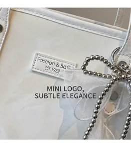 Detail einer weißen Ledertasche mit Mode-Logo und dekorativer Schleife aus Organza