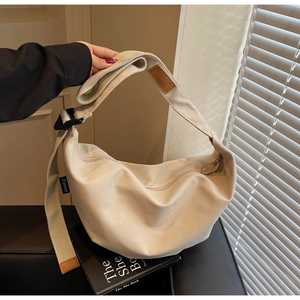 Detail of adjustable strap and leather patch on beige canvas half-moon shoulder bag