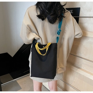 Détails d'un sac seau en toile noire minimaliste avec bandoulières jaune et bleu