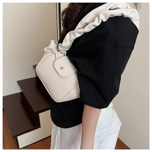 Detail of cream pleated shoulder strap and silver magnetic closure on a small handbag