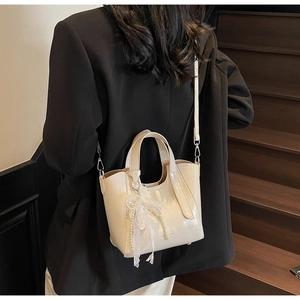 Close-up of cream white glossy bucket bag with pearl lace bow detail and shoulder strap