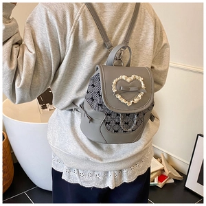 Detail of grey mini backpack with bow and lace heart on model in a cozy indoor setting