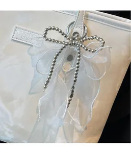 Detail einer silbernen Perlenkette mit weißer Organza-Schleife an einer Marmortasche