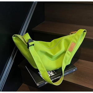 Detail of neon green canvas crossbody bag with adjustable strap and logo on wooden stairs