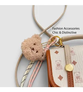 Close-up of the beige leather crossbody bag with teddy bear pattern and plush keychain