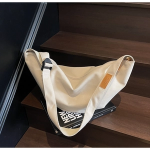 Detail of a beige canvas crescent bag with a brown leather label on wooden stairs