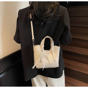 Chic cream leather bucket bag with lace bow and pearl charm shown in a commuting scene