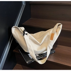 Detail of cream canvas dumpling bag showing the leather logo tag and wide shoulder strap