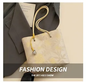 Macro detail of beige tote bag with embossed flowers, yellow braided rope, and silver bell