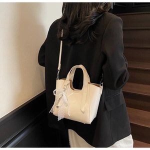 Detail of cream white mini tote bag with pearl lace bow charm on model wearing black suit