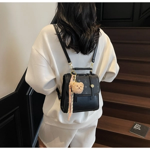 Detailed back view of a black vintage backpack with bear charm on a wooden staircase
