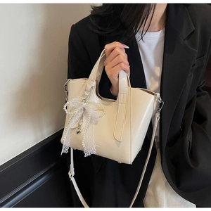 Close-up of cream bucket bag with pearl lace bow and metallic heart pendant detail
