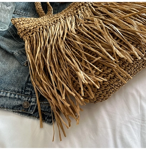 Détail du sac de plage en paille avec franges bohèmes posé sur une veste en jean bleue